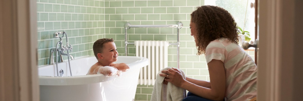 Child in bath, adult smiling.